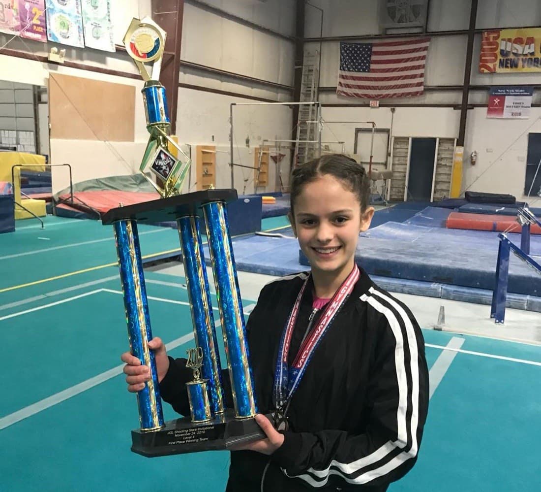 A young gymnast holding a first-place team trophy